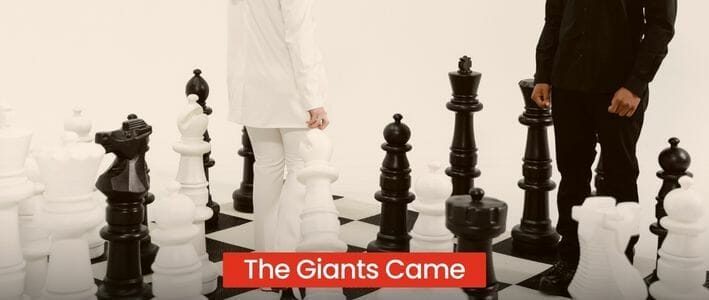 Two Men Standing On A Giant Chess Board